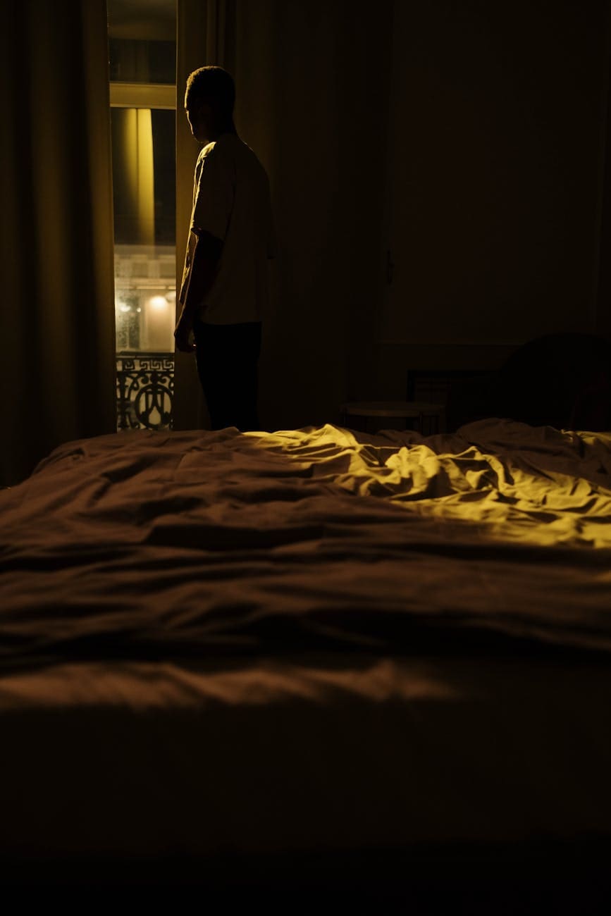 silhouette of person standing by window in bedroom at night